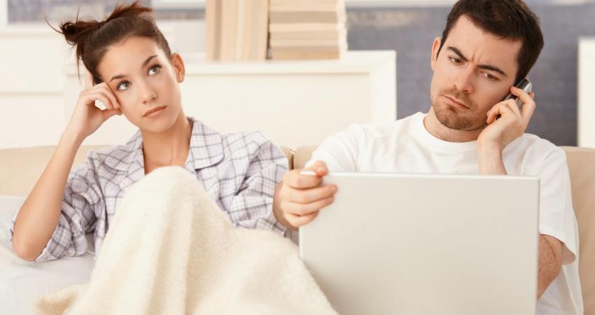 young-couple-in-bed-man-working-woman-bored